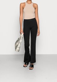 Beige ärmlös bodysuit, svarta vida byxor, svarta slidesandaler och en vit handväska i ormskinnsmönster med ett rektangulärt spänne.