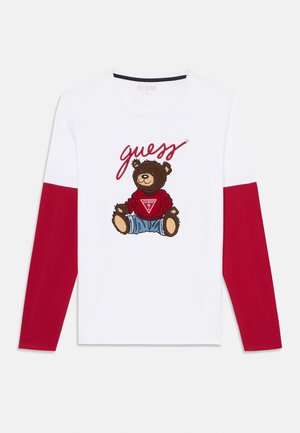 Hvit langermet T-skjorte med design av en brun bjørn i rød genser og blå jeans, med røde ermer og teksten 'guess' over.