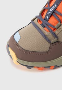 Κοντινό πλάνο στο μπροστινό μέρος παπουτσιού πεζοπορίας με επάνω μέρος σε μπεζ, καφέ και πορτοκαλί, μπλε κορδόνια και υφή πολύχρωμης σόλας, με σήμα Terrex.