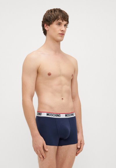 Μπλέ σκούρο ανδρικό μποξεράκι με λευκή και κόκκινη ζώνη με λογότυπο Moschino; λεία υφή, εφαρμοστό σ�χέδιο και μήκος μέχρι το μέσο του μηρού.