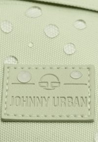 Light green textured fabric featuring water droplets; a beige embossed label with "JOHNNY URBAN" and circular design elements.