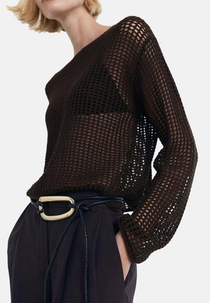 Bruine opengebreide trui met lange mouwen, gecombineerd met high-waisted donkere broeken en een zwarte gevlochten riem met een gouden gespdetail.