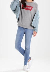 Felpa grigia con logo rosso Levi's, giacca azzurra chiara, jeans skinny azzurri chiari e sneakers bianche. Tessuto morbido con jeans leggermente strappati.