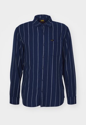 Camicia a maniche lunghe blu navy con strisce bianche verticali, chiusura a bottoni e una tasca sul petto. Realizzata in tessuto morbido con colletto.