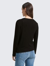 Zwarte top met lange mouwen en ronde hals, met een gladde textuur en een relaxed fit, gecombineerd met lichtblauwe jeans met achterzakken.