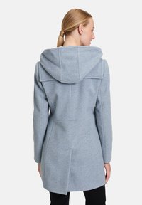 Lichtblauwe wollen jas met capuchon, heeft een getailleerde pasvorm, verticale naden en een lengte tot halverwege de dij. Gelaagd stof met een zachte afwerking.