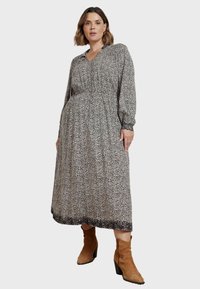 Lång klänning i svart och vitt mönster med elastiska manschetter, v-ringning och indragen midja. Till detta bärs bruna mocka ankelboots.