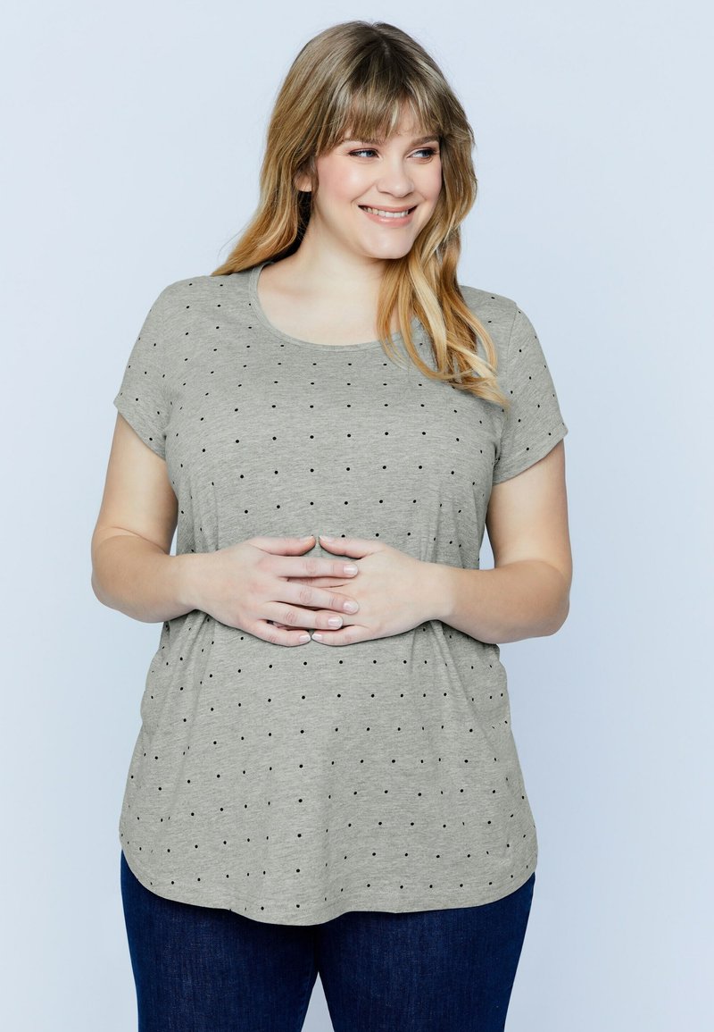 Camiseta corta de manga con un tono gris claro y un escote redondeado, con un patrón de puntos negros en toda la prenda y un corte relajado, con un dobladillo ligeramente curvado.