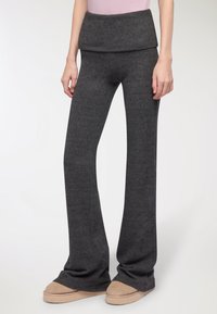 Rozszerzane ciemnoszare dzianinowe spodnie z szerokim, zawijanym pasem, charakteryzujące się miękką teksturą i luźnym krojem, stylizowane z jasnobrązowym obuwiem.