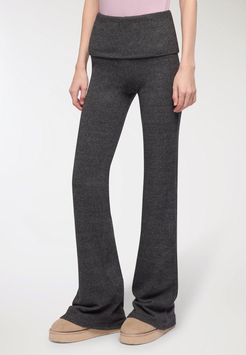 Rozszerzane ciemnoszare dzianinowe spodnie z szerokim, zawijanym pasem, charakteryzujące się miękką teksturą i luźnym krojem, stylizowane z jasnobrązowym obuwiem.