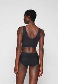 Black sports bra with wide straps and low scoop back, paired with a matching high-waisted bottom, smooth fabric and minimal design.