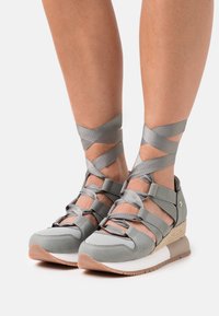 Zapatillas deportivas grises con correas cruzadas, material texturizado, suela en cuña y suela de goma. Presentan un detalle tejido en el talón.