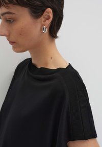 Top nero in tessuto morbido, con distintivi dettagli a coste sulle spalle e design a barca. Orecchini d'argento completano il look.
