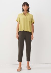 Camicetta a maniche corte, di colore giallo chiaro, con colletto e chiusura a bottoni, abbinata a pantaloni tapered verde scuro e sandali infradito beige.