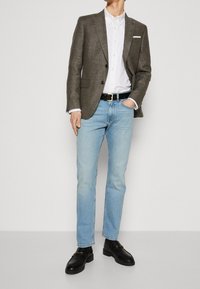 Blazer gris, chemise blanche, jeans bleu clair, ceinture noire et mocassins noirs. Le blazer possède deux boutons et un mouchoir de poche. Textures lisses.