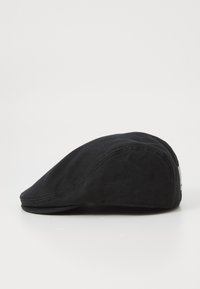 Cappello flat nera con visiera curva e dettaglio di tessuto cucito, appoggiato su una superficie bianca, visto di lato.