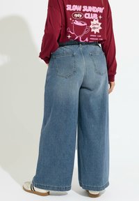Szerokie, jasnoniebieskie dżinsy z tylnymi kieszeniami i wysokim stanem. W połączeniu z bordową bluzką z długim rękawem z nadrukiem graficznym.
