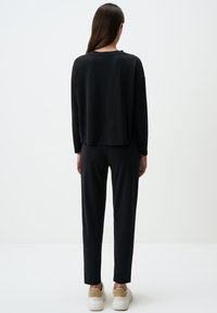 Schwarzes langärmeliges Oberteil und dazu passende schmale Hose, aus weichem Stoff. Einfaches Design mit lässiger Passform, kombiniert mit weißen Sneakers.