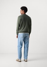 Grøn sweatshirt med rund hals, parret med lyseblå jeans og beige sneakers. Glat tekstur og afslappet pasform. Minimalistisk design.