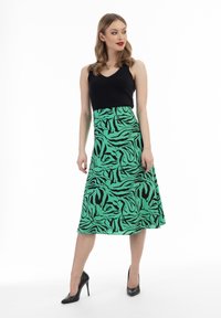 Mouwloze zwarte top, gecombineerd met een groene rok met zwarte abstracte patronen. Model draagt zwarte hoge hakschoenen; gladde stof en vloeiende ontwerp.