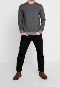 Grå stickad tröja med rund halsringning, ribbade muddar och fåll. Kombinerad med svarta byxor och bruna läderstövlar.