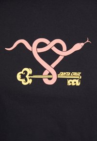 Maglietta nera con un serpente rosa intrecciato a una chiave gialla, con "SANTA CRUZ" stampato in giallo sotto il design.
