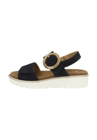 Sandalo in suede blu navy con una larga fascetta anteriore, una fascia posteriore regolabile e un grande accento circolare. Presenta una suola bianca e texturizzata.