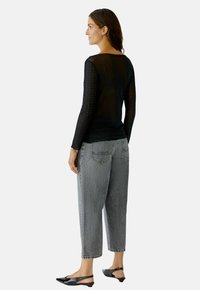 Schwarzes, langärmeliges, durchscheinendes Oberteil mit gepunkteter Textur, kombiniert mit lässigen grauen Jeans im Denim-Stil und schwarzen Slingback-Schuhen. Sichtbare Rückendetails.