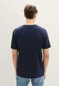 Camiseta de algodón de color azul marino, con mangas cortas, cuello redondo y una textura suave. Diseño liso en la parte posterior, mostrado en una persona.