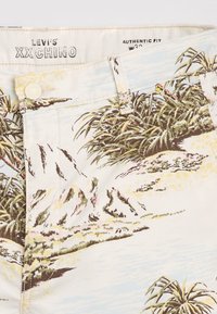 Pantalon chino blanc Levi’s avec motif tropical, fermeture par bouton, passants pour ceinture, et étiquettes "XX CHINO" et taille W32 à l'intérieur de la ceinture.