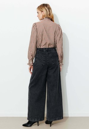 Femme vue de dos portant un chemisier à carreaux marron et blanc rentré dans un jean denim noir taille haute et jambes larges, ainsi que des bottes noires à talons.