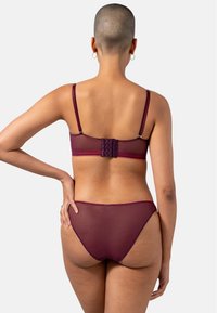 Burgundy läpikuultav aluskleit, mis sisaldab lühikese rinnahoidjaga, millel on õhukesed rihmad ja klõpsuga sulgemine, koos sobivate bikiinistiilis aluspükstega.