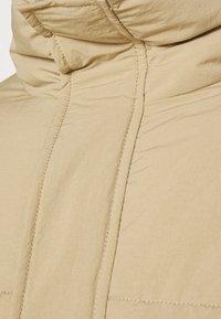 Beige puffer jacket featuring a high collar, visible stitching, and crinkled texture. Soft, lightweight material designed for warmth.