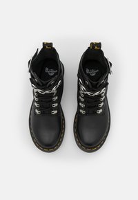 Coppia di stivaletti Dr. Martens neri in pelle con lacci, cuciture gialle e occhielli in metallo, vista dall'alto su sfondo bianco.