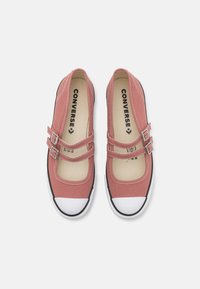 Zapatos de lona rosa estilo Mary Jane con correas de doble hebilla, punteras de goma blanca y suelas de goma negra. Presentan costuras en contraste.