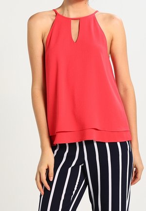 Haut sans manches corail avec un col en forme de clé, conception superposée et tissu léger. Associé à un pantalon rayé vertical noir et blanc.