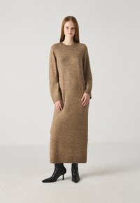 Long, brown knit dress with a crew neckline, full sleeves, and ribbed cuffs. Paired with black pointed-toe heeled boots.