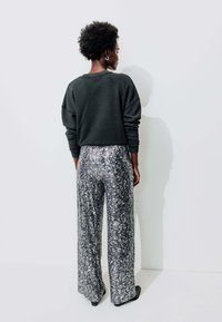 Sweatshirt noir oversize avec épaules tombantes associé à un pantalon large en métal argenté et noir à motif. Tissu lisse, détails minimalistes.