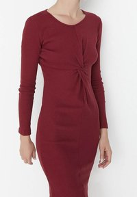 Robe bordeaux à manches longues, présentant une texture côtelée, une silhouette ajustée et un détail torsadé à l'avant. Tissu lisse avec une longueur midi.