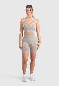 Světlý šedý sportovní set zahrnující přiléhavý sportovní top s tenkými ramínky a kalhoty s vysokým pasem, vyrobený z měkkého, hladkého materiálu.