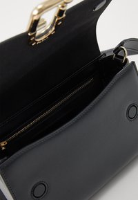 Borsa a mano in pelle nera con hardware dorato, dotata di apertura superiore e tasca interna con zip, texture liscia e accenti circolari.