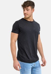 Crni pamučni T-shirt s okruglim izrezom, kratkim rukavima i opuštenim krojem. Blago zakrivljen rub, meka tekstura i minimalni detalji šivanja.