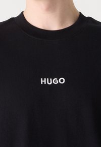 Schwarzes Baumwoll-T-Shirt mit klassischem Rundhalsausschnitt und gesticktem "HUGO"-Logo in Weiß auf der Brust. Weicher Stoff, lässige Passform.