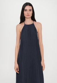 Abito halter blu scuro con pieghe verticali, silhouette fluida e scollatura rotonda. Realizzato in tessuto morbido, presenta una trama lunga e liscia.