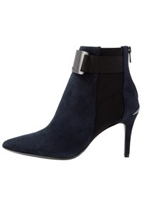 Bottine en daim bleu marine avec bout pointu, talon aiguilles, et panneau élastique noir contrastant ; ornée d'un détail boucle métallique.