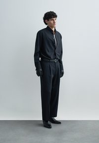 Black button-up shirt with a high collar, paired with loose-fitting black trousers. Accessories include black gloves and shoes, presenting a monochrome look.