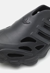 Svart glidsko i texturerad gummi, med flera ventilationshål och en framträdande logotyp, i en strömlinjeformad och böjd design.