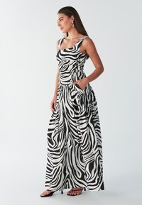 Abito lungo con stampa a zebra bianco e nero, caratterizzato da un corpetto aderente, scollatura quadrata, tasche laterali e gonna fluente. Realizzato in tessuto leggero.