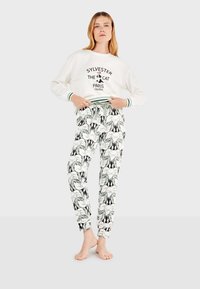 Weißer Pullover mit schwarzem Druck und grünen Akzenten, kombiniert mit gemusterten Schlafanzughosen, die Sylvester den Kater in Schwarz-Weiß zeigen.