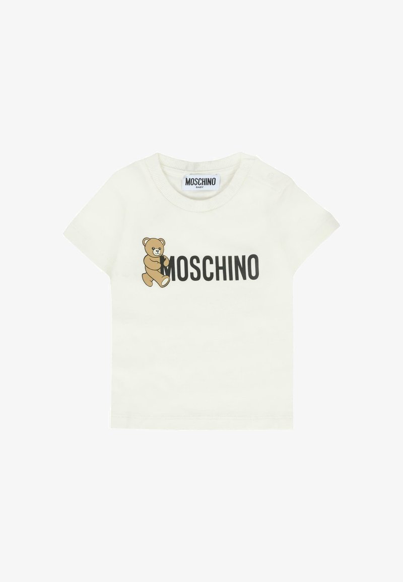 Biała dziecięca koszulka z grafiką misia teddy obok grubego czarnego napisu "MOSCHINO" z przodu oraz z napami na ramieniu.